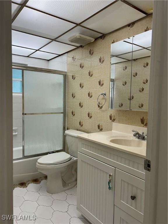 bathroom featuring vanity, visible vents, shower / bath combination with glass door, tile walls, and toilet