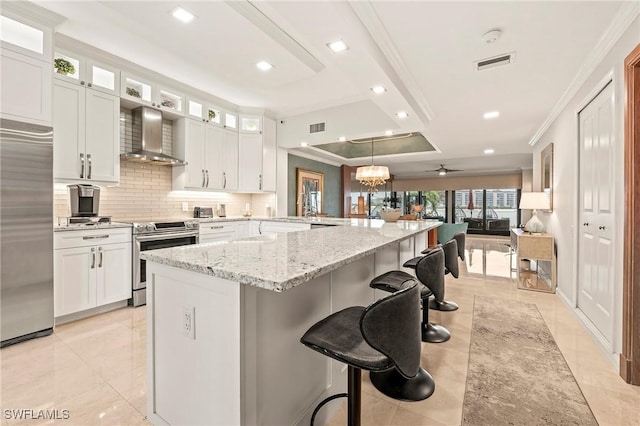 kitchen with a kitchen breakfast bar, appliances with stainless steel finishes, wall chimney range hood, and white cabinetry