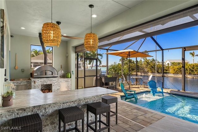 exterior space featuring an outdoor kitchen, a lanai, a bar, and a water view