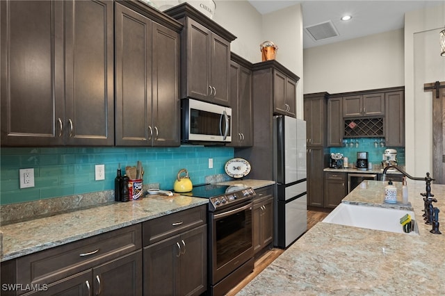 kitchen featuring light stone countertops, light wood-type flooring, dark brown cabinetry, stainless steel appliances, and sink