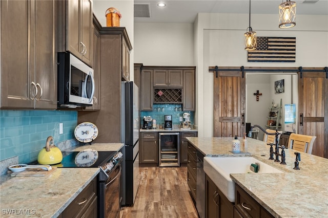 kitchen with appliances with stainless steel finishes, a barn door, light stone counters, and beverage cooler