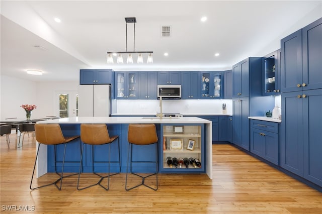 kitchen with white appliances, blue cabinetry, and an island with sink