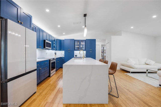 kitchen featuring stainless steel appliances, blue cabinets, lofted ceiling, a kitchen breakfast bar, and hanging light fixtures