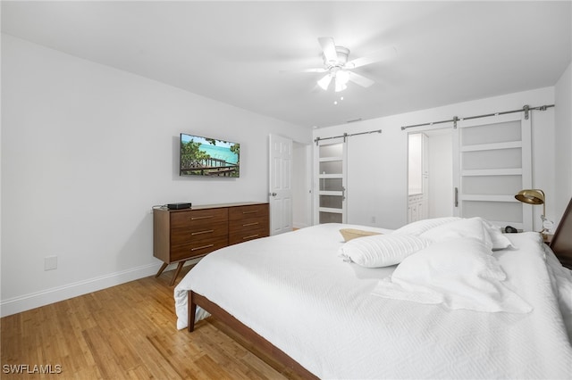 bedroom with ceiling fan, a barn door, and light hardwood / wood-style flooring