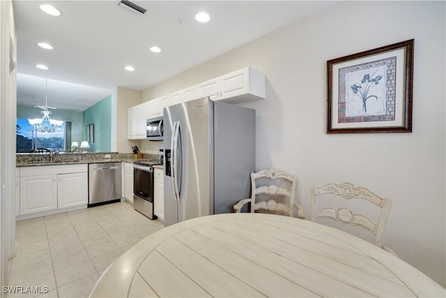 kitchen featuring appliances with stainless steel finishes, a notable chandelier, dark stone countertops, white cabinets, and sink