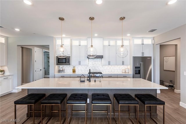 kitchen featuring dark wood-type flooring, a large island with sink, appliances with stainless steel finishes, and a kitchen breakfast bar