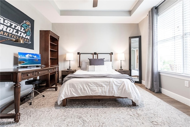 bedroom with ceiling fan, a tray ceiling, and light hardwood / wood-style flooring