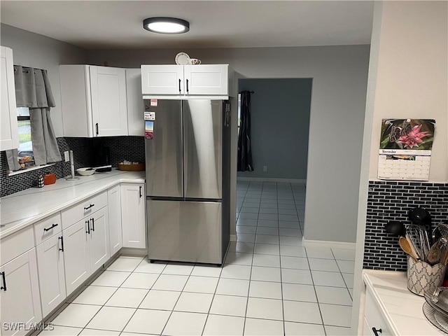 kitchen featuring light countertops, light tile patterned flooring, freestanding refrigerator, and white cabinets