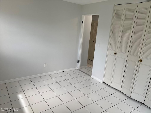 unfurnished bedroom with light tile patterned floors, a closet, and baseboards