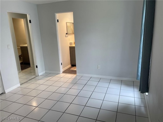 unfurnished bedroom with light tile patterned flooring, connected bathroom, and baseboards