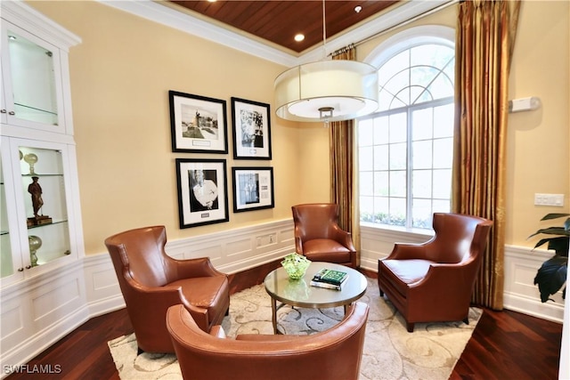 living area with a decorative wall, wainscoting, wood finished floors, and ornamental molding