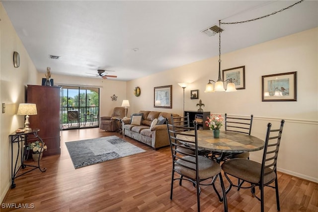 dining space with ceiling fan with notable chandelier and hardwood / wood-style flooring