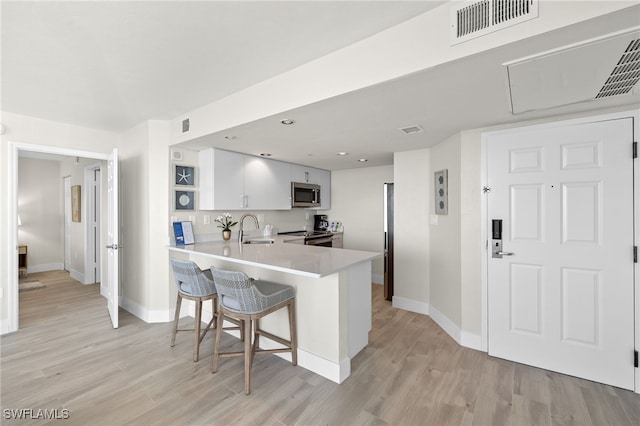 kitchen featuring kitchen peninsula, a kitchen bar, stainless steel appliances, sink, and white cabinetry