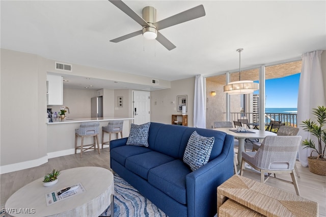 living room with floor to ceiling windows, ceiling fan, light hardwood / wood-style flooring, and a water view