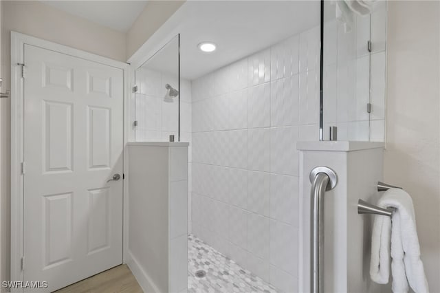 bathroom with a tile shower and wood-type flooring