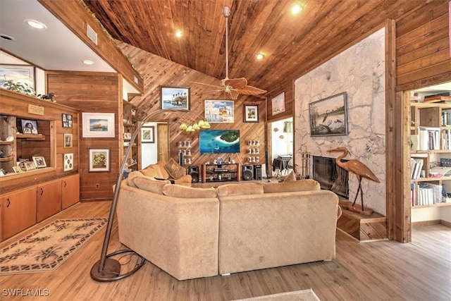 living room with wooden ceiling, wooden walls, vaulted ceiling with beams, a fireplace, and light hardwood / wood-style floors