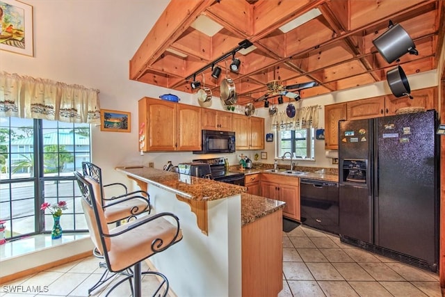 kitchen featuring dark stone counters, black appliances, sink, a kitchen bar, and kitchen peninsula