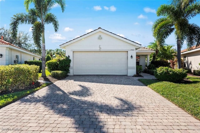 single story home with a garage, decorative driveway, a tiled roof, and stucco siding