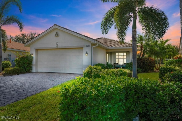 ranch-style house featuring a garage, a tile roof, decorative driveway, and stucco siding