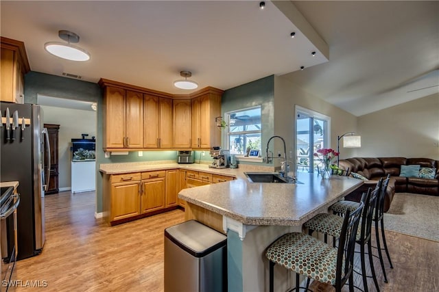 kitchen with stainless steel refrigerator, sink, a kitchen breakfast bar, light hardwood / wood-style flooring, and kitchen peninsula