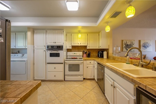 kitchen featuring white appliances, sink, white cabinets, washing machine and dryer, and hanging light fixtures