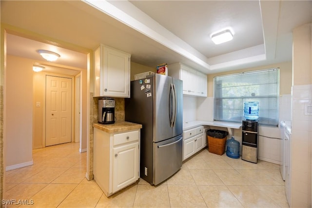 kitchen featuring stainless steel fridge, a tray ceiling, light tile patterned floors, white cabinetry, and tile counters