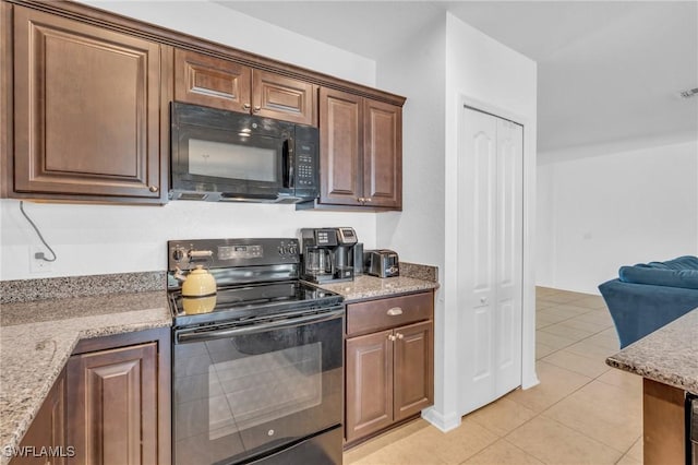 kitchen featuring light tile patterned floors, light stone counters, and black appliances