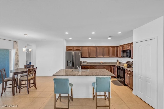 kitchen featuring a kitchen island with sink, sink, black appliances, and decorative light fixtures