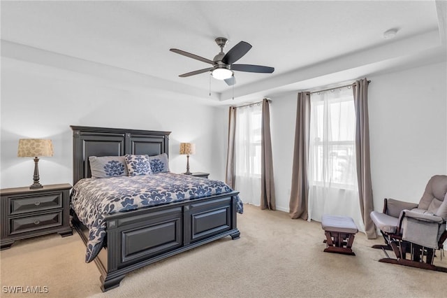 carpeted bedroom with ceiling fan and a tray ceiling