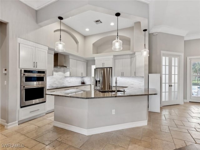 kitchen with wall chimney range hood, white cabinetry, hanging light fixtures, stainless steel appliances, and dark stone counters