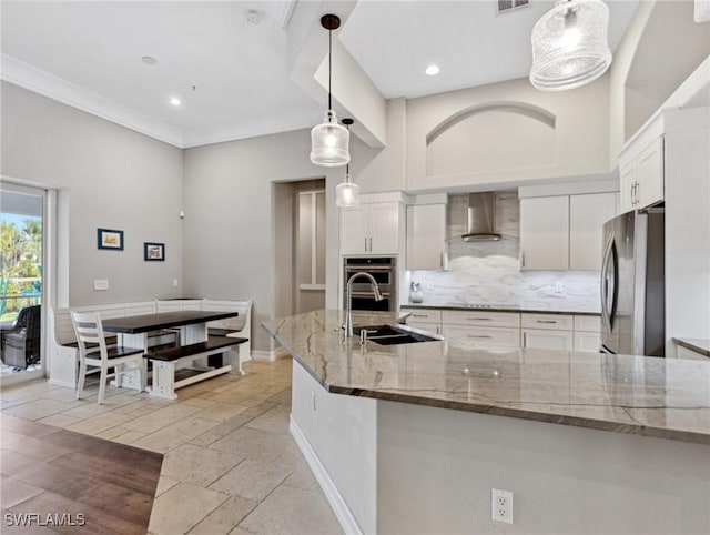 kitchen featuring wall chimney range hood, sink, hanging light fixtures, stainless steel appliances, and white cabinets