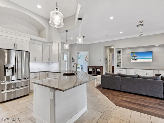 kitchen featuring stainless steel refrigerator with ice dispenser, light stone countertops, pendant lighting, white cabinets, and sink