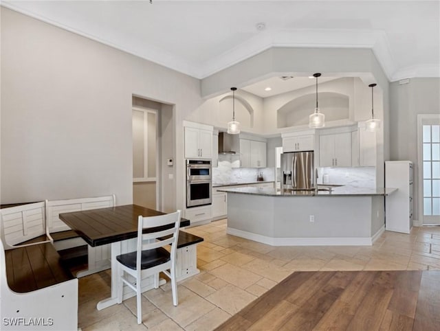 kitchen with white cabinetry, stainless steel appliances, decorative backsplash, decorative light fixtures, and wall chimney range hood