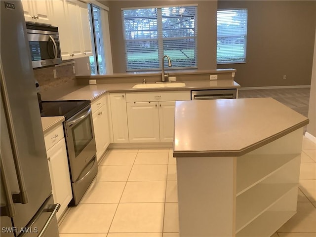 kitchen featuring sink, stainless steel appliances, light tile patterned floors, a kitchen island, and white cabinets