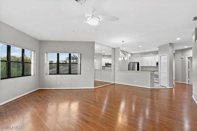 unfurnished living room featuring ceiling fan with notable chandelier and dark hardwood / wood-style floors