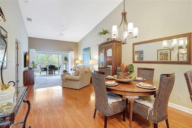 dining space with high vaulted ceiling, ceiling fan with notable chandelier, and light hardwood / wood-style flooring