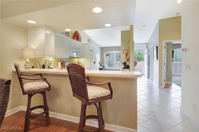 kitchen with kitchen peninsula, white appliances, a kitchen breakfast bar, lofted ceiling, and white cabinets