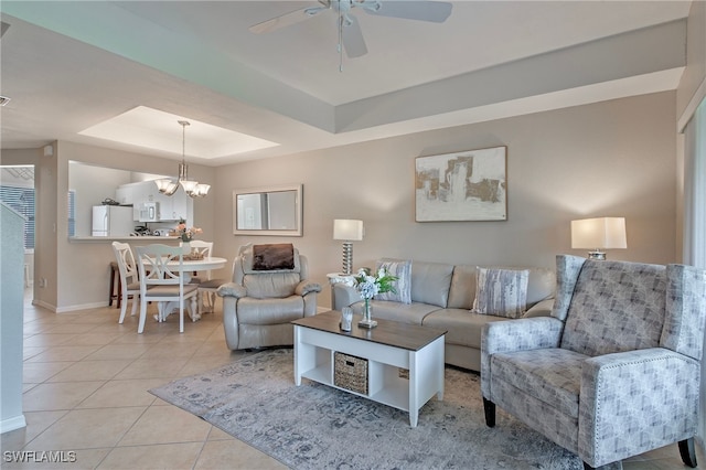 tiled living room with ceiling fan with notable chandelier and a raised ceiling