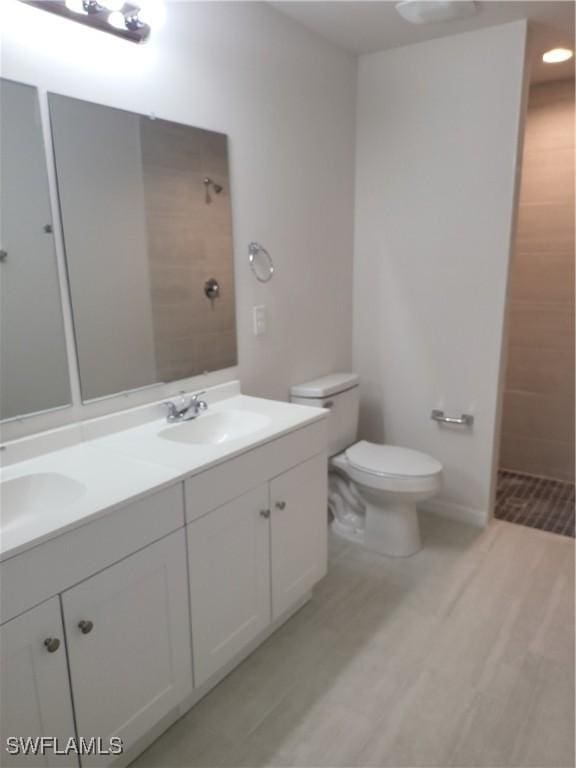 bathroom featuring hardwood / wood-style floors, vanity, toilet, and a tile shower