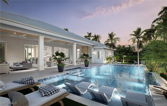 pool at dusk with pool water feature, ceiling fan, and a patio