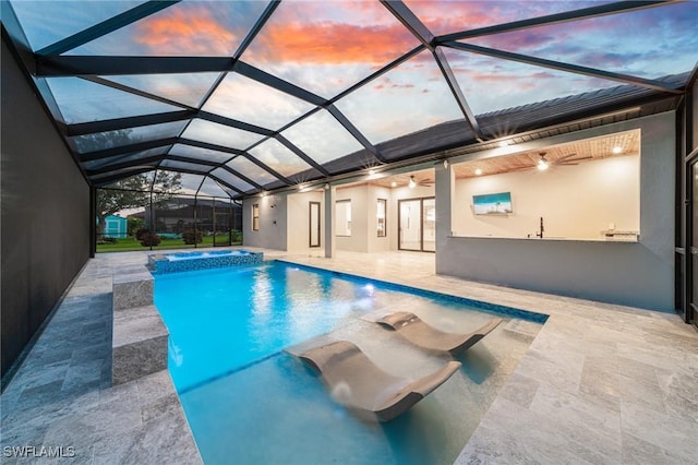 pool at dusk with glass enclosure, an in ground hot tub, and a patio area