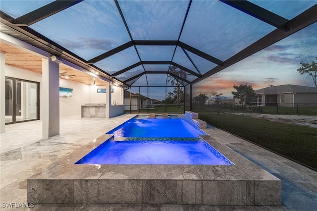 pool at dusk featuring pool water feature, glass enclosure, an in ground hot tub, and a patio