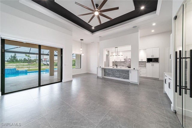 unfurnished living room with ceiling fan, a raised ceiling, and a towering ceiling