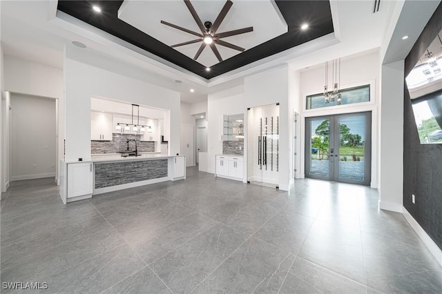 unfurnished living room featuring ceiling fan with notable chandelier, french doors, sink, and a tray ceiling