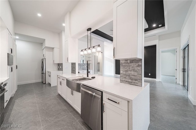 kitchen featuring pendant lighting, backsplash, sink, white cabinetry, and stainless steel appliances