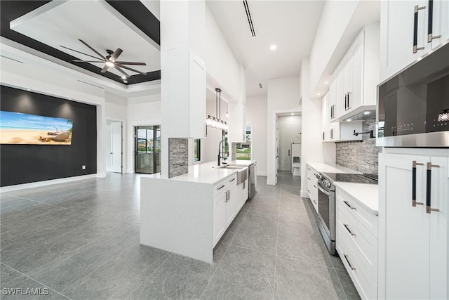 kitchen with ceiling fan, stainless steel appliances, a towering ceiling, decorative light fixtures, and white cabinets