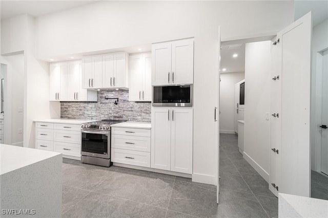 kitchen with white cabinets, dark tile patterned floors, built in microwave, stainless steel range, and tasteful backsplash