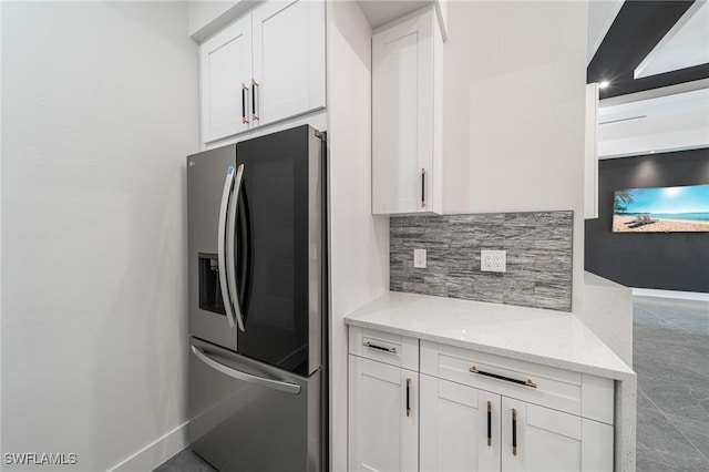 kitchen with backsplash, light stone countertops, white cabinets, and stainless steel refrigerator with ice dispenser