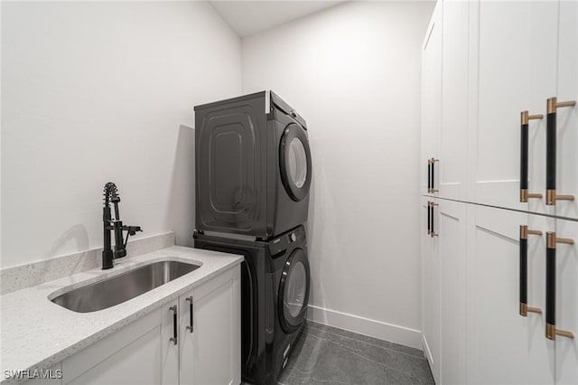 clothes washing area with stacked washer and dryer, cabinets, dark tile patterned flooring, and sink