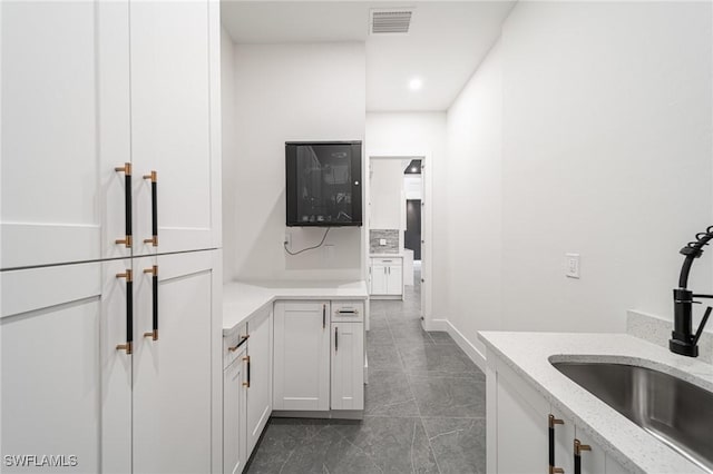 kitchen featuring backsplash, light stone counters, white cabinetry, and sink